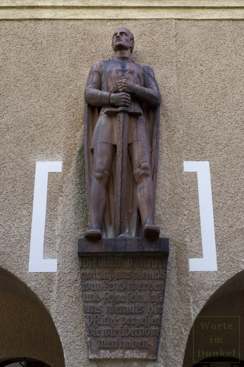 Terrakotta-Figur in Gestalt eines schwerttragenden Kriegers an der Fassade des Thuryhofs – darunter ein Spruch von Adolf Hitler.