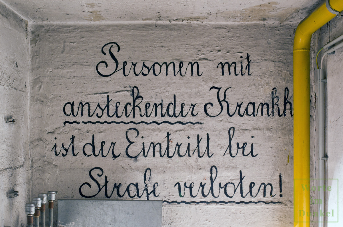 Aufschrift über dem Abgang in einen Bunker: "Personen mit ansteckender Krankheit ist der Eintritt bei Strafe verboten!"